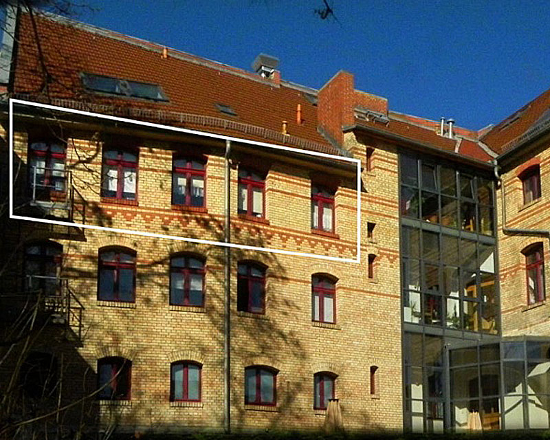 Von aussen sieht man den gelben Backstein mit roten Schmuckziegeln und rote Holz-Fenster